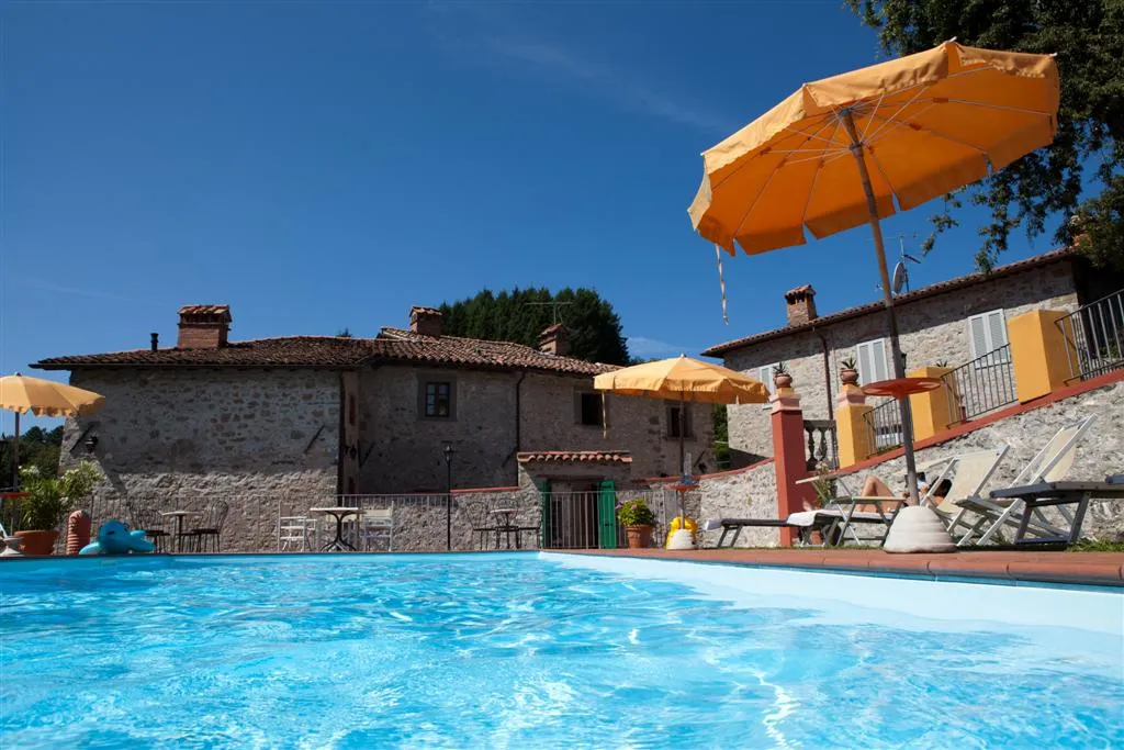 Piscina dell’agriturismo con ombrelloni arancio e il casale in pietra